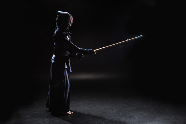 Vue latérale du combattant kendo en armure pratiquant avec épée de bambou sur noir
 - Photo, image