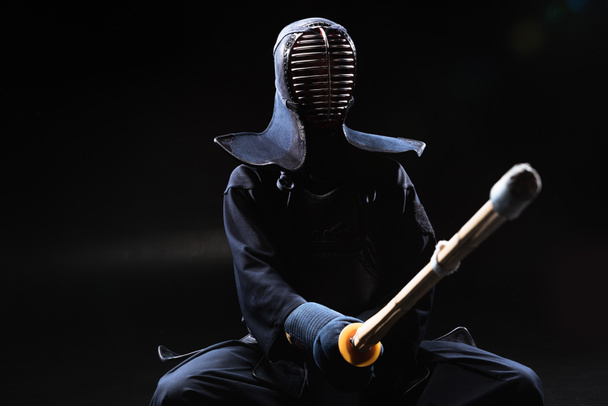 Kendo fighter in helmet holding bamboo sword on black - Fotó, kép