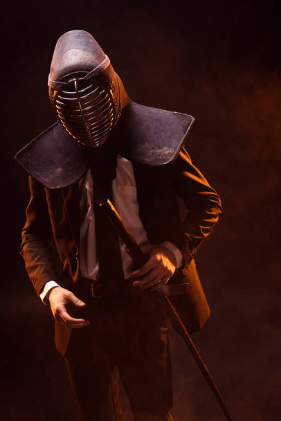 Kendo lutador em desgaste formal e capacete segurando espada de bambu no escuro
 - Foto, Imagem