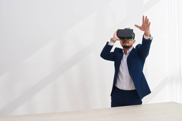 Mature entrepreneur asiatique portant des lunettes de réalité virtuelle pour contrôler le travail de ses employés
 - Photo, image