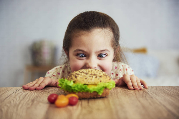 Hravá dívka při pohledu na lahodný hamburger - Fotografie, Obrázek