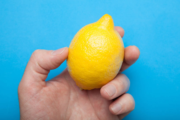 A man's hand holds a juicy yellow lemon on a blue background. - Fotoğraf, Görsel
