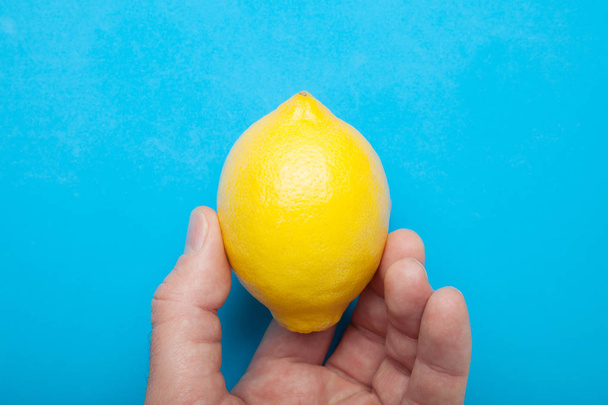Ripe yellow lemon in hand, close-up. Isolated on a blue backgrou - Fotoğraf, Görsel