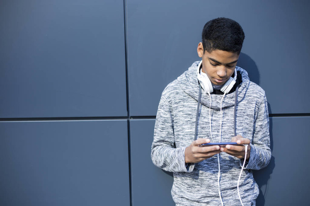 νέος άνθρωπος στα ακουστικά ακούγοντας μουσική σε ένα smartphone. Αφρικανός Αμερικανός τύπος παίζοντας ένα παιχνίδι σε ένα κινητό τηλέφωνο. - Φωτογραφία, εικόνα