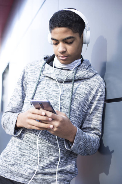 jeune homme en casque écoutant de la musique sur un smartphone. Afro-américain gars jouer à un jeu sur un téléphone mobile
. - Photo, image