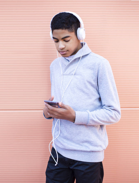 joven con auriculares escuchando música en un smartphone. chico afroamericano jugando un juego en un teléfono móvil
. - Foto, Imagen