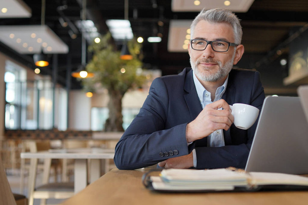 Mature businessman smiling during working coffee break - Фото, изображение