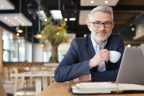 Mature businessman smiling at camera during working coffee break - Foto, Imagen