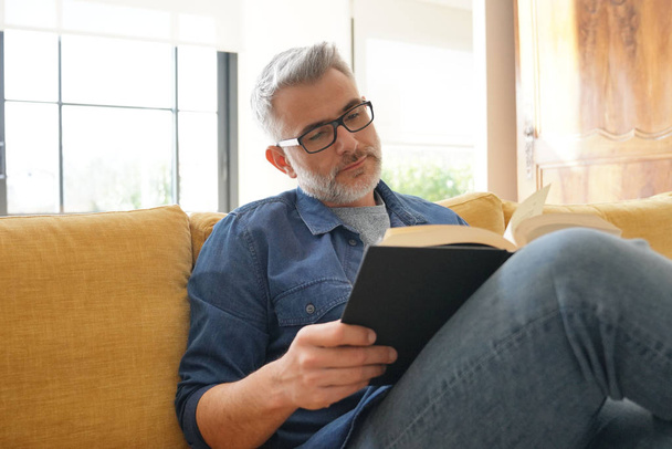 Man in 40s reading book in modern home - Foto, afbeelding