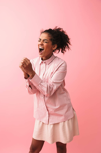 Beautiful young african woman posing isolated over pink wall background screaming singing. - Foto, immagini