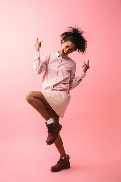 Beautiful young african woman posing isolated over pink wall background screaming. - 写真・画像