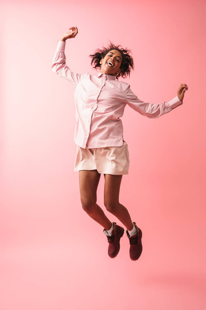 Beautiful young african woman posing isolated over pink wall background jumping. - Foto, Imagem