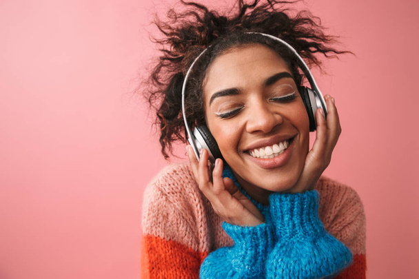 Όμορφη νεαρή γυναίκα αφρικανική θέτοντας απομονωμένες πάνω φόντο ροζ τοίχο ακούτε μουσική με ακουστικά. - Φωτογραφία, εικόνα