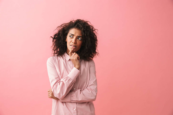 Thinking beautiful young african woman posing isolated over pink wall background dressed in pajama. - 写真・画像