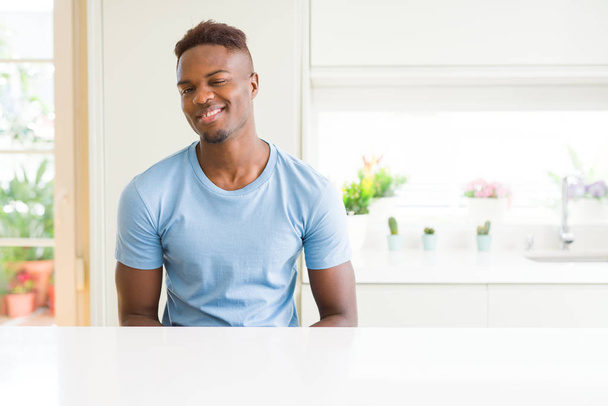 schöner afrikanisch-amerikanischer Mann in lässigem T-Shirt zu Hause zwinkernd in die Kamera blickend mit sexy Ausdruck, fröhlichem und glücklichem Gesicht. - Foto, Bild