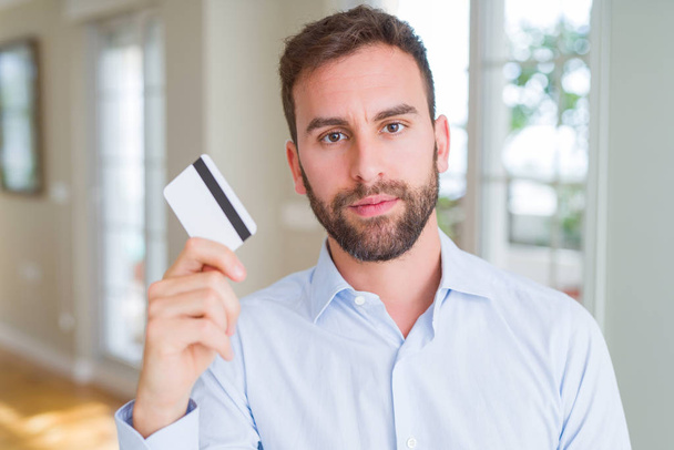 Beau homme d'affaires tenant la carte de crédit avec une expression confiante sur la pensée intelligente visage sérieux
 - Photo, image