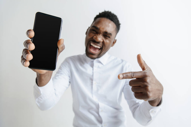 Indoor portrait of attractive young black african man isolated on pink background, holding blank smartphone, smiling at camera, showing screen, feeling happy and surprised. Human emotions, facial - Фото, зображення