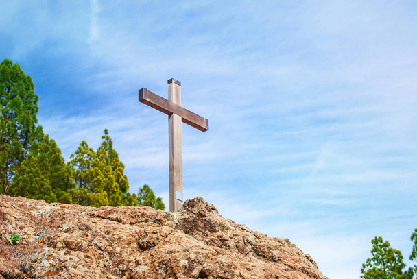 Wooden Christian cross towers on a stone rock on the background of a blue sky with clouds - Photo, Image