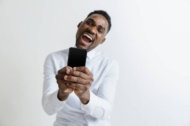 Indoor portrait of attractive young black african man isolated on pink background, holding blank smartphone, smiling at camera, showing screen, feeling happy and surprised. Human emotions, facial - Fotó, kép