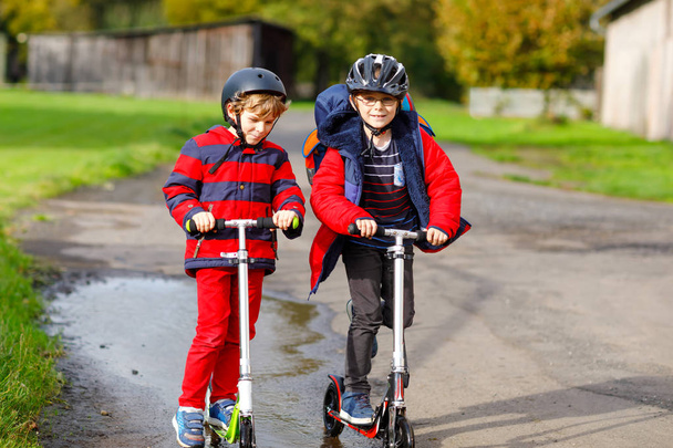 Zwei kleine Jungen auf dem Weg zur oder von der Schule. Schüler im Alter von 7 Jahren fahren durch Regenpfützen. Lustige Geschwister und beste Freunde spielen zusammen. Kinder gehen zur Schule. - Foto, Bild