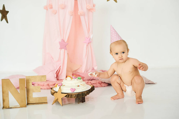A little baby in a pink tent with a magic wand near a big cake.  - Fotó, kép