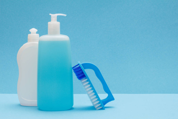 Bottles of dishwashing liquid and brush on blue background. - Фото, зображення
