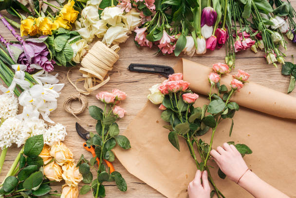 Partial view of florist making flower bouquet on wooden surface - Foto, afbeelding