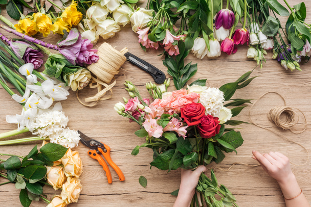 Cropped view of florist holding bouquet of fresh flowers on wooden surface - Foto, Imagem