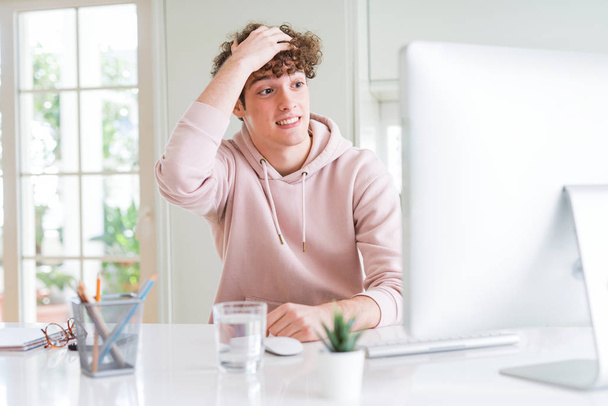 Young student man using computer stressed with hand on head, shocked with shame and surprise face, angry and frustrated. Fear and upset for mistake. - Foto, Imagen