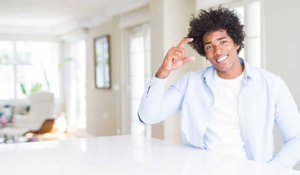 Američan Afričana muž doma usměvavé a sebevědomý ukázal rukou dělá velikost cedulka s prsty při pohledu a fotoaparát. Opatření koncepce. - Fotografie, Obrázek