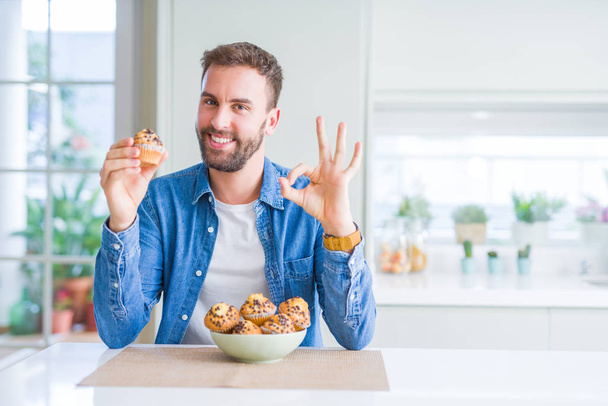 Handsome man eating chocolate chips muffin doing ok sign with fingers, excellent symbol - Photo, Image