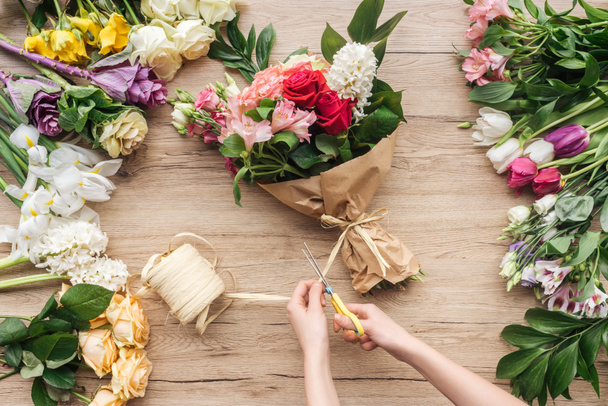 Cropped view of florist making flower bouquet on wooden surface - Foto, afbeelding
