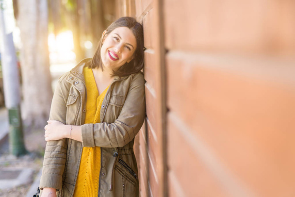 Krásná mladá žena s úsměvem sebevědomá a vesele se opírá o dřevěné zdi, chůze na ulici města za slunečného dne - Fotografie, Obrázek