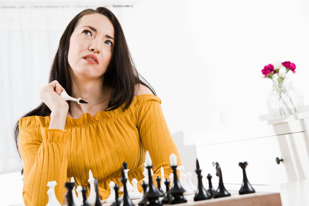Γυναίκα σε κίτρινο φόρεμα συνεδρίαση μπροστά από σκάκι - μετακινήσετε το βασιλιά. - Φωτογραφία, εικόνα