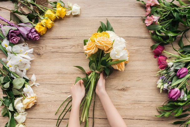 Partial view of florist holding bouquet of fresh flowers on wooden surface - Foto, Imagen