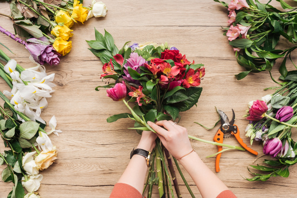 Cropped view of florist making flower bouquet on wooden surface - Foto, Imagem