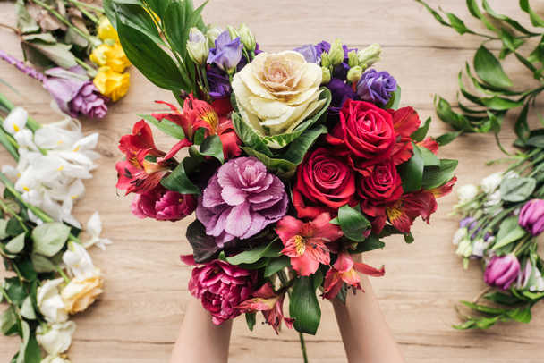 Partial view of florist holding bouquet of fresh flowers on wooden surface - Foto, Imagem