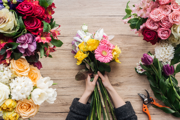 Cropped view of florist making flower bouquet on wooden surface - Foto, Imagen