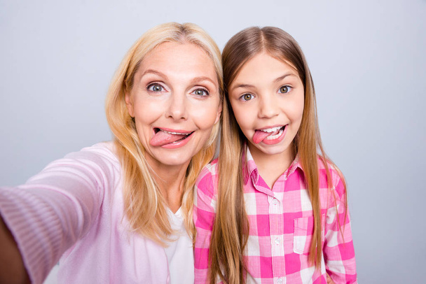 Close up photo cheer two people blond haired she her granny little daughter make take selfies tongue out mouth weekend wear pink plaid checkered shirt sweater pullover isolated light grey background - Фото, зображення