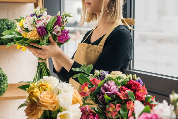 Vista cortada de florista em avental segurando buquê na loja de flores
 - Foto, Imagem