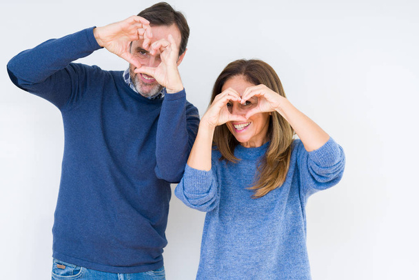 Beautiful middle age couple in love over isolated background Doing heart shape with hand and fingers smiling looking through sign - Fotografie, Obrázek