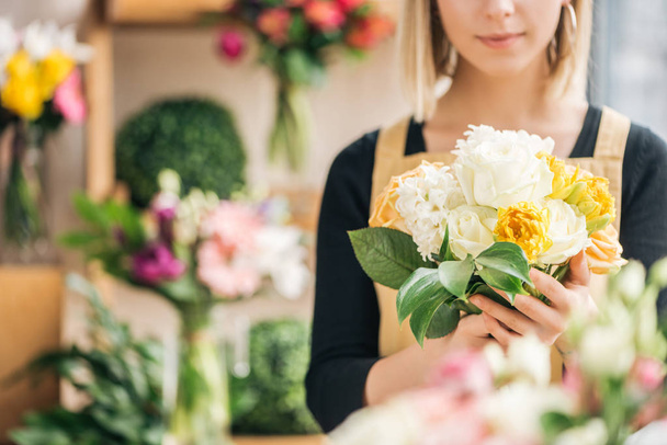 Cropped view of florist in apron holding bouquet in flower shop - Fotó, kép