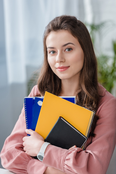 Atractivo estudiante de camisa rosa sosteniendo cuadernos con sonrisa
 - Foto, imagen