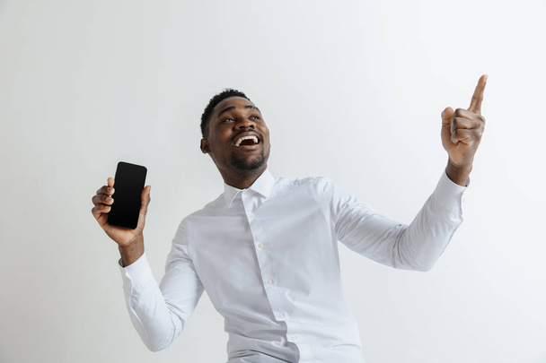 Indoor portrait of attractive young black african man isolated on pink background, holding blank smartphone, smiling at camera, showing screen, feeling happy and surprised. Human emotions, facial - Zdjęcie, obraz