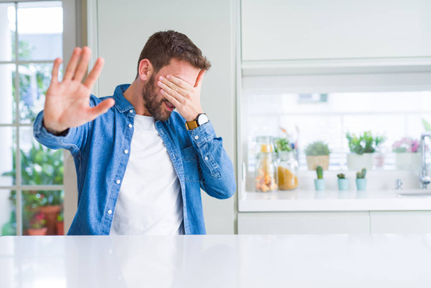 Handsome man at home covering eyes with hands and doing stop gesture with sad and fear expression. Embarrassed and negative concept. - Foto, imagen
