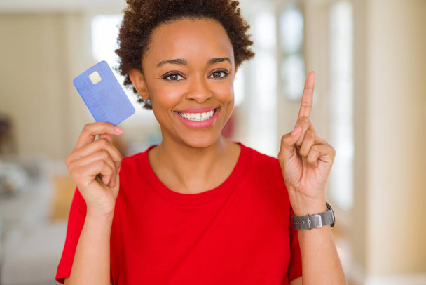 Jonge african american vrouw met creditcard verrast met een idee of vraag wijzende vinger met blij gezicht, nummer één - Foto, afbeelding