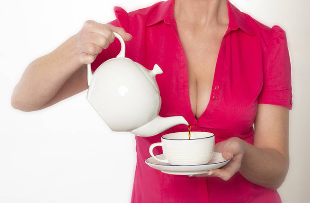 Южная Англия Великобритания. около 2018 года. Привлекательная женщина в обнаженной красной рубашке, наливающей чашку чая
 - Фото, изображение