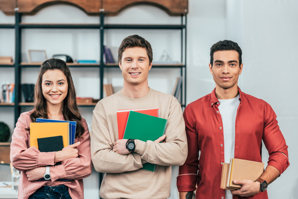 Three multiethnic students holding notebooks and books and looking at camera - Foto, Imagem
