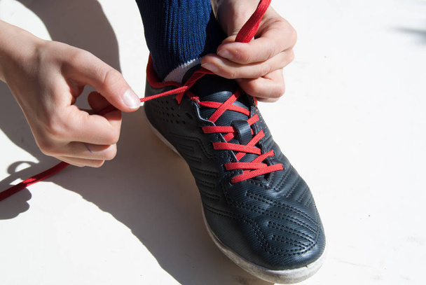 Primer plano de las manos de un niño atando un zapato de fútbol sobre fondo blanco
 - Foto, imagen