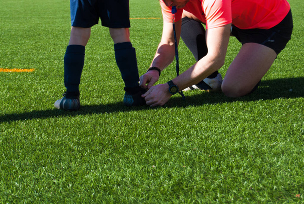 Árbitro atando un zapato a un jugador de fútbol infantil
 - Foto, imagen